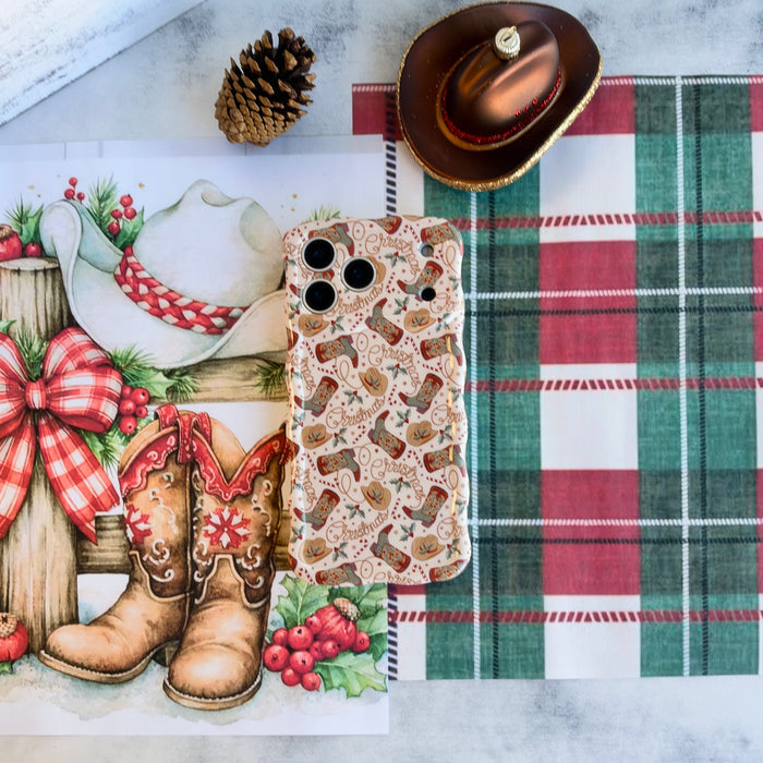 Boot Scootin' Christmas iPhone case lying flat on red and green plaid beside watercolor cowboy boots and a cowboy hat ornament