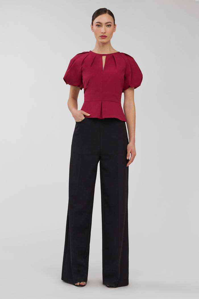 Woman wearing a red blouse and black pants on a gray background