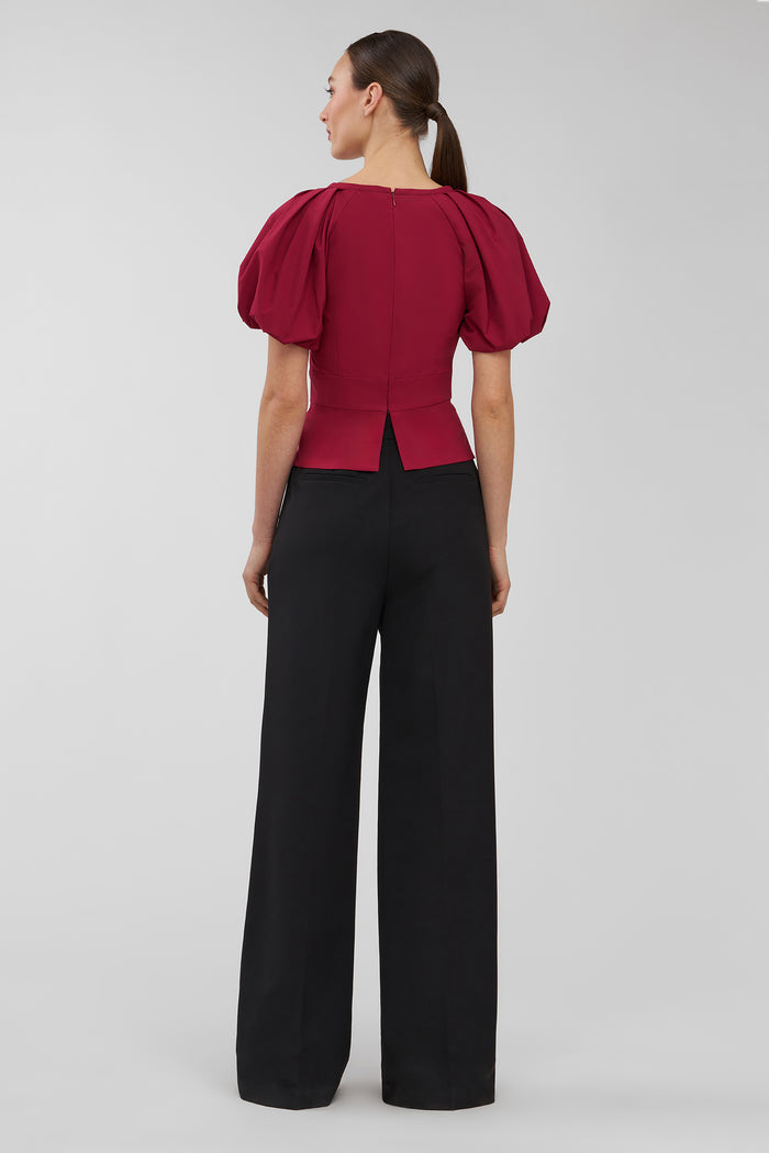 Woman wearing a red blouse with puff sleeves and black pants on a gray background