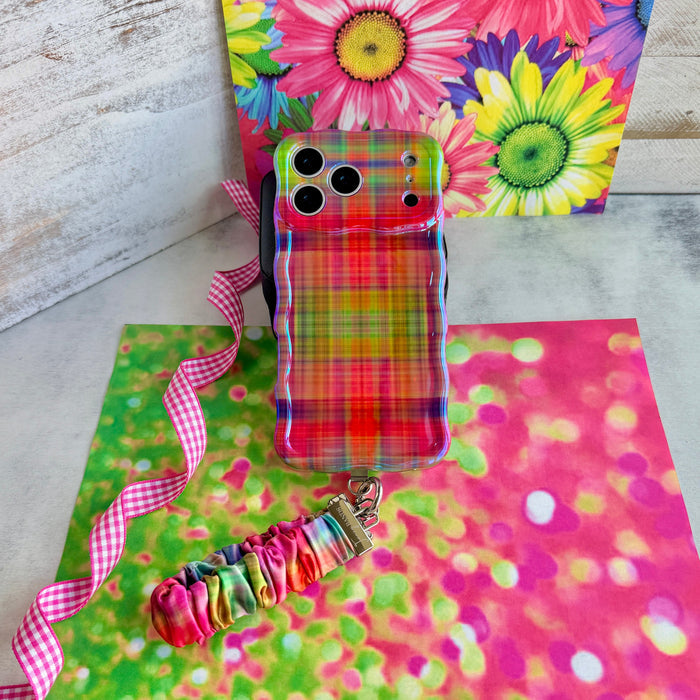 Hazy Tartan scrunchie phone wrist strap laid out with the matching blurred rainbow plaid Wavy Luxe iPhone case on a daisy print backdrop