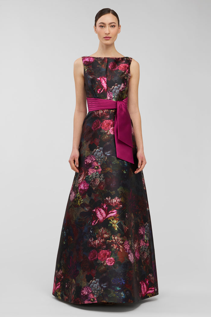 Woman wearing a floral evening gown with a pink belt on a gray background