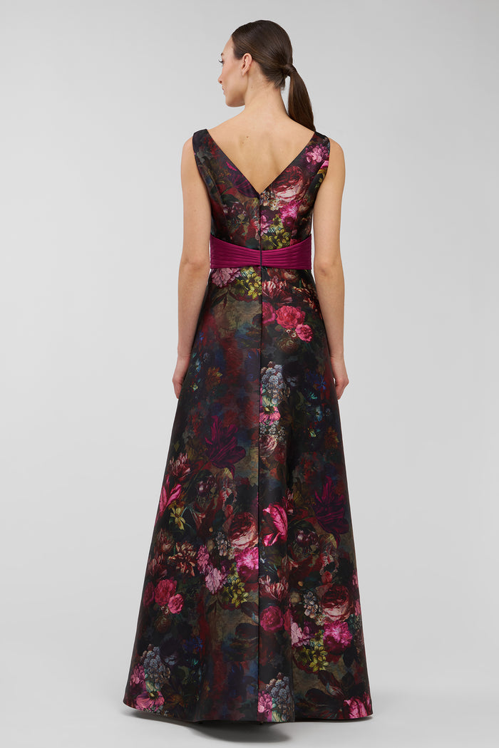 Woman wearing a floral evening gown with a deep neckline and belt on a light gray background