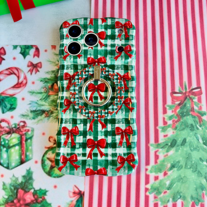Close-up of the Plaid Tidings & Bows MagSafe grip ring on the matching gingham bow iPhone case, on red and white striped paper