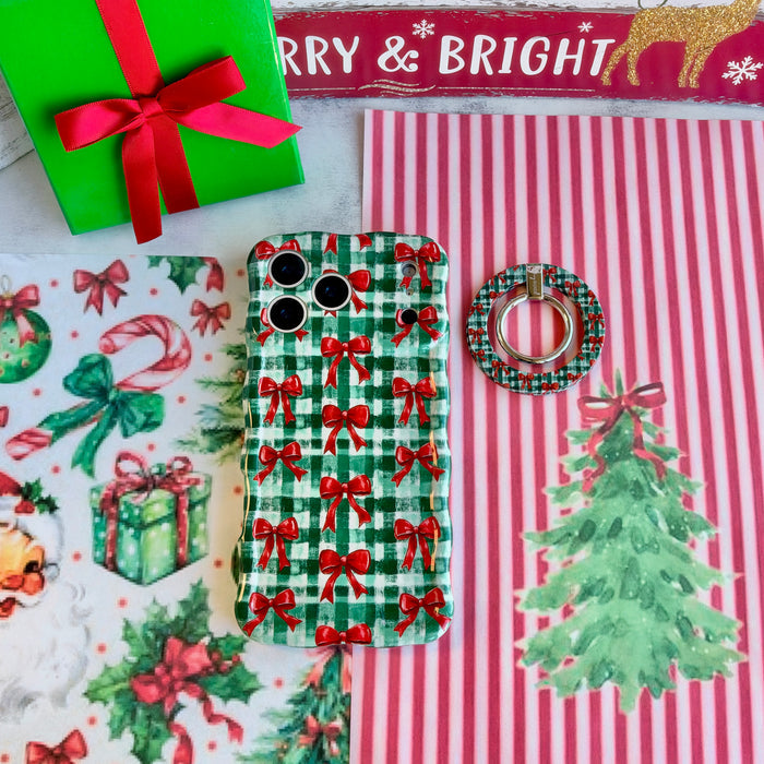 Plaid Tidings & Bows MagSafe grip ring lying beside the matching iPhone case with a green gift box and Merry & Bright sign