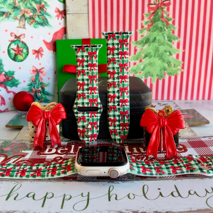 Plaid Tidings & Bows Apple Watch band shown on an Apple Watch and as two straps on a black jewelry box, red bows on green gingham