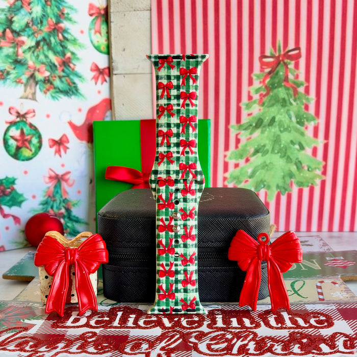 Plaid Tidings & Bows Apple Watch band buckled and standing on a black jewelry box between red bow ornaments