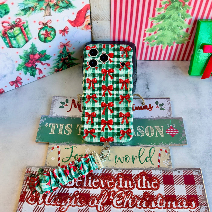 Plaid Tidings & Bows iPhone case and gingham bow scrunchie wrist strap on stacked wooden Christmas signs with a green gift box