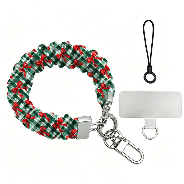 Plaid Tidings & Bows scrunchie phone wrist strap laid flat with silver clasp and phone tab, red bows on green gingham
