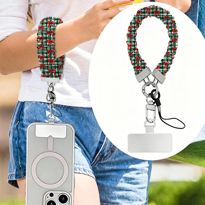 Plaid Tidings & Bows scrunchie phone strap worn on the wrist with an iPhone hanging from it, plus close-up of the strap and phone tab