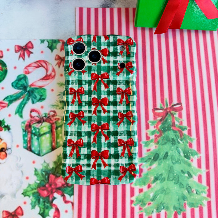 Plaid Tidings & Bows iPhone case lying flat on red and white striped paper beside a watercolor Christmas tree