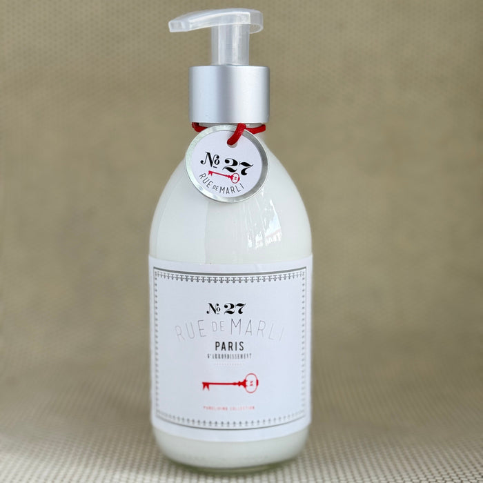 glass bottle of rue de marli body lotion with white label on neutral background.