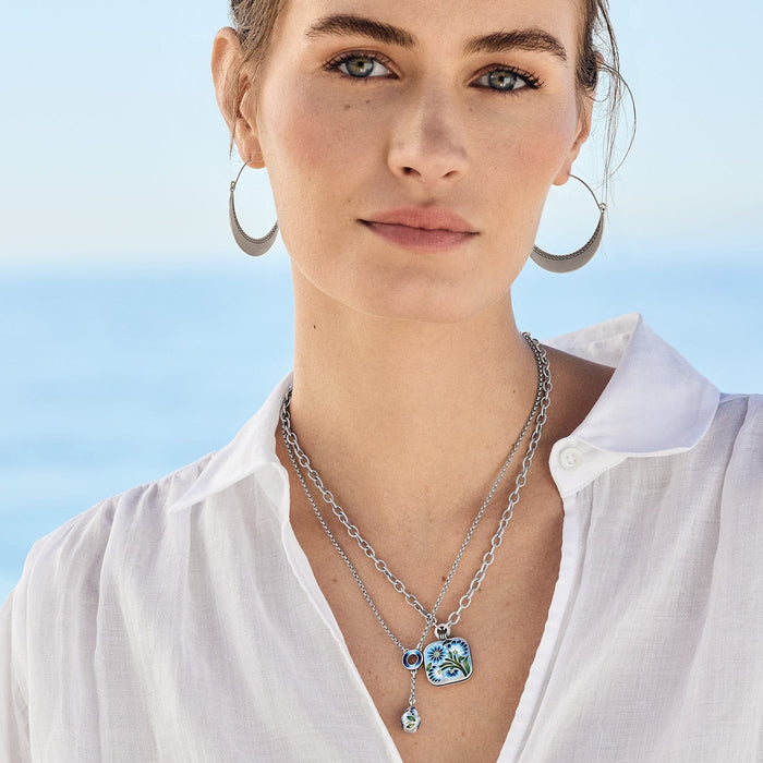 Model wearing a Brighton silver-plated layered necklace with blue enamel floral pendant and coordinating Brighton accessories