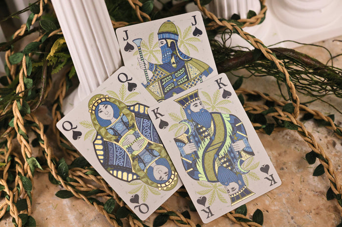Three Court Cards with decorative designs on a textured surface with greenery.