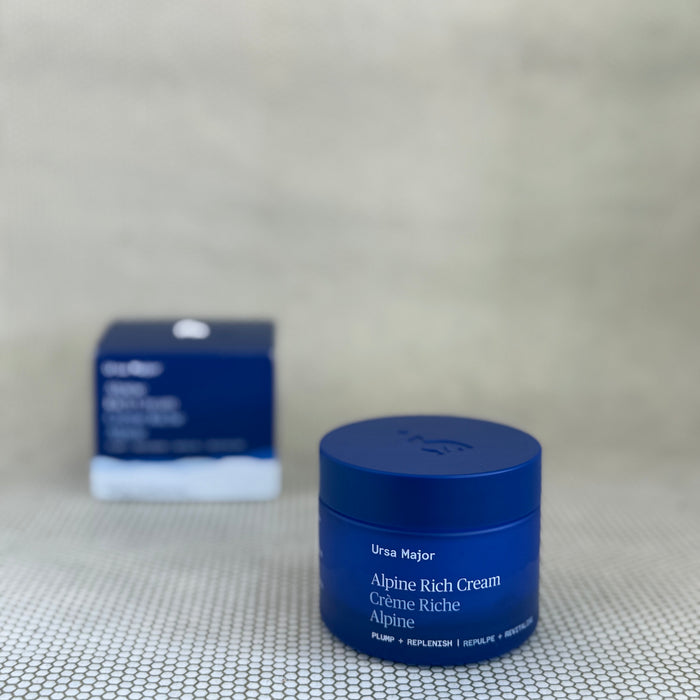 Blue jar of Ursae Major Alpine Rich Cream on a textured surface with a blurred box in the background.