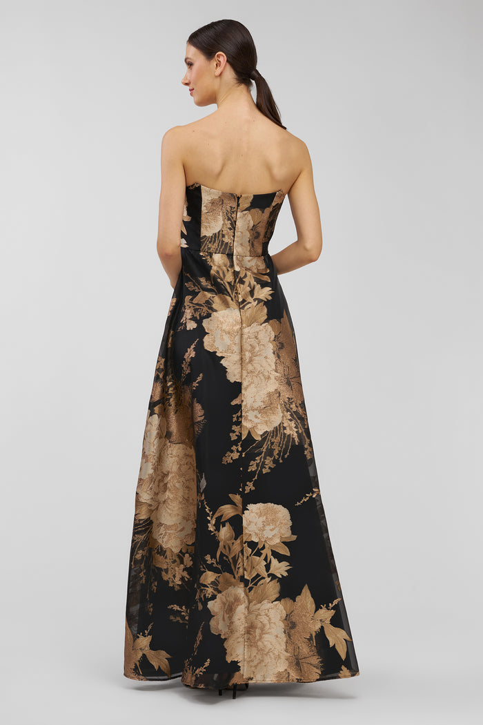 Woman wearing a strapless floral evening gown on a plain background