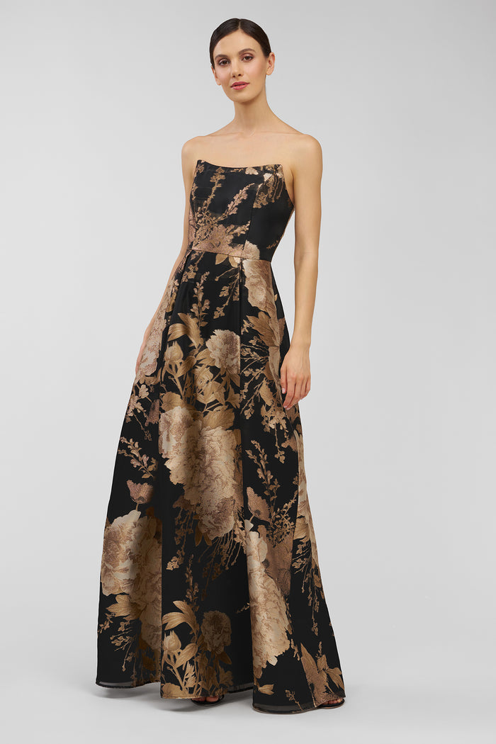Woman wearing a strapless, long dress with a black and brown abstract pattern on a white background