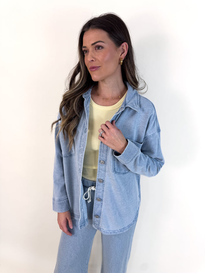 Woman wearing a light blue denim jacket over a yellow top on a white background