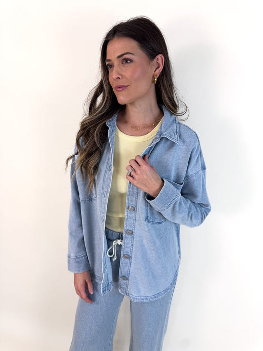 Woman wearing a light blue denim jacket over a yellow top on a white background